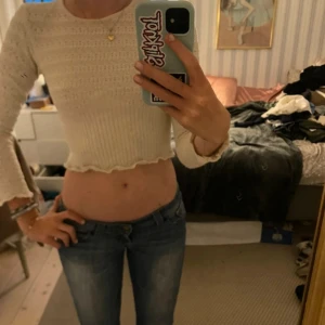 Vit croppad stickad topp - Supersöt vit croppad stickad topp med lång ärm och vågig kant nertill. Toppen har ett diskret hålmönster och sitter inte tajt och bekvämt. Perfekt för dig som gillar en feminin och trendig stil.