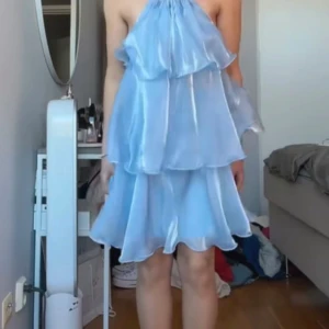 Ljusblå volangklänning från Fenty - Säljer en drömmig ljusblå kortklänning från Fenty med flera lager volanger och halterneck med knyt i nacken. Klänningen är tillverkad i 100% polyester och endast använd 1gång.