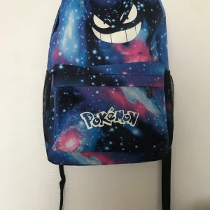 Nattlysande Pokémon ryggsäck - Snygg ryggsäck med Pokémon-tryck och coolt galaxmönster i blått, rosa och svart. Framsidan har ett stort Gengar-ansikte och Pokémon-loggan. Ryggsäcken har justerbara axelremmar, sidofickor i mesh och dragkedja framtill. Perfekt för skolan eller häng med kompisar. Helt ny 