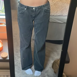 NA-KD low straight jeans - Säljer ett par mörkgråa jeansbyxor från NA-KD med klassisk femficksdesign och raka ben. Byxorna har låg midja och vita sömmar som kontrast. Perfekta för en avslappnad och trendig look. Är typ uppsprättade där nere men fick de så! Inget som påverkar användningen. 699 nya!!