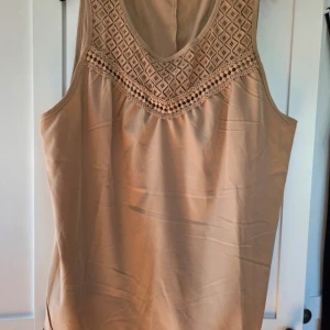 Beige blus med spets från SHEIN - Säljer en beige blus från SHEIN Curve med snygg spetsdetalj och broderat mönster upptill. Blusen är ärmlös och har en lös passform, perfekt för varma dagar. Materialet är mjukt och lätt, vilket gör den superbekväm att bära.