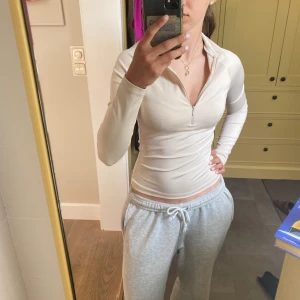 Beige långärmad half zip topp - Säljer en beige långärmad topp med half zip framtill och hög krage. Modellen är tight och har en stilren, enkel look som passar perfekt till jeans eller träningsbyxor. Materialet känns mjukt och stretchigt, vilket gör den riktigt skön att bära.