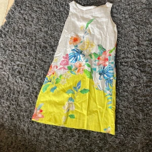 Vit och gul blommig långklänning Zara Girls - Säljer en superfin långklänning från Zara Girls i storlek 164. Klänningen är vit upptill och övergår i en härlig gul färg nedtill, med färgglatt blommigt mönster i blått, rött, grönt och orange. Ärmlös modell med v-ringad detalj framtill, perfekt för sommarens alla tillfällen.
