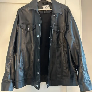 Svart jacka från NA-KD - Snygg svart jacka från NA-KD med klassisk krage, tryckknappar och två bröstfickor. Materialet är slätt och glansigt med silverfärgade knappar. Inga defekter och är som ny💕