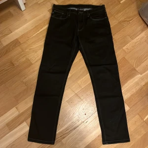 Svarta jeans från Armani - Snygga svarta jeans från Armani med klassisk femficksdesign och silverfärgad logga på bakfickan. Jeansen har raka ben och kontrasterande sömmar som ger en stilren vibe. Perfekta för dig som gillar en clean och modern look.