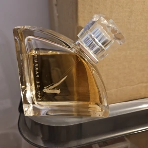 Valentino Eau de Parfum 90ml - Lyxig parfym från Valentino i en unik, asymmetrisk glasflaska med transparent design och silvrig detalj på korken. Innehåller 90 ml gyllene Eau de Parfum. Flaskan har ett stilrent V-tryck på framsidan och känns riktigt exklusiv.