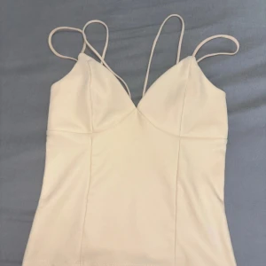 Beige ribbad linnetopp med smala band - Säljer en snygg beige linnetopp med dubbla smala axelband och v-ringad front. Toppen är ribbad och har en figurnära passform som framhäver siluetten. Perfekt att styla med jeans eller kjol för en trendig look.