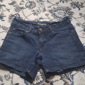 Mörkblå jeansshorts från Vila - Snygga mörkblå jeansshorts från Vila med klassisk femficksdesign, bälteshällor och knappstängning i metall. Shortsen har raka ben och är perfekta för en chill sommarlook. Materialet är robust denim som håller formen hela dagen.
