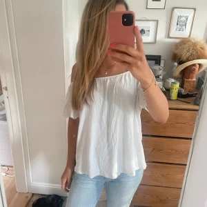 Vit offshoulder blus med spetsdetaljer - Säljer en luftig vit blus med offshoulder-modell och korta ärmar. Har en litet märke på tröjan som sytts ihop men syns knappt när man har på den! Pris kan diskuteras!