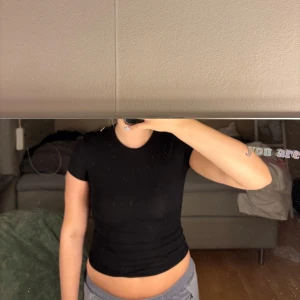 Svart croppad t-shirt - En enkel svart croppad t-shirt med tight passform och korta ärmar. Perfekt att matcha med jeans eller mjukisbyxor för en avslappnad look.