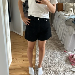 Svarta jeansshorts med normal passform - Snygga svarta jeansshorts med klassisk femficksdesign och knappstängning fram. Shortsen har en rak och normal passform, perfekt för dig som gillar enkel och stilren look. Passar grymt till t-shirt eller hoodie och är ett måste i garderoben.