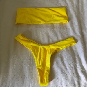 Gul bandeau bikini - Snygg gul bikini med bandeau-topp och högt skurna trosor. Enkel och stilren design som verkligen poppar på stranden. Perfekt för dig som vill sticka ut med en färgglad look i sommar.