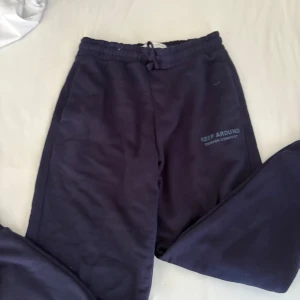 Mörkblå mjukisbyxor från Zara - Säljer ett par mörkblå mjukisbyxor från Zara med trycket 'KEEP AROUND' på ena benet. Byxorna har elastisk midja med snörning och är gjorda i mjukt bomullsmaterial. Perfekta för chill dagar eller träning.