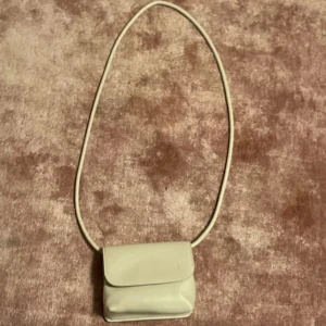 Beige axelväska från Zara - Säljer en stilren beige axelväska från Zara med minimalistisk design. Väskan har ett smidigt lock och lång axelrem, perfekt för att bära det viktigaste. Tillverkad i syntetmaterial med en clean look som passar till många outfits.