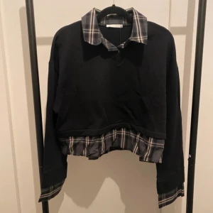 Svart croppad tröja med rutig detalj Zara - Svart croppad tröja från Zara med rutig skjortkrage och rutiga detaljer vid ärmslut och nederkant. Tröjan har lång ärm och en loose passform, perfekt för dig som gillar lager-på-lager-looken. Snygg kontrast mellan det svarta och de grå rutorna.