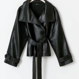 Svart skinnjacka med bälte från Gina Tricot - Snygg svart skinnjacka från Gina Tricot. Helt slutsåld, perfekt inför hösten.