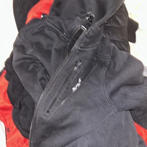 Svart fleecejacka från sailracing - Svart fleecejacka från sail racing med dragkedja och hög krage. Jackan har en enkel design med en bröstficka med dragkedja och är perfekt för kyliga dagar. Mjuk och skön insida i fleece som håller dig varm. Passar dig som gillar en clean och sportig stil.