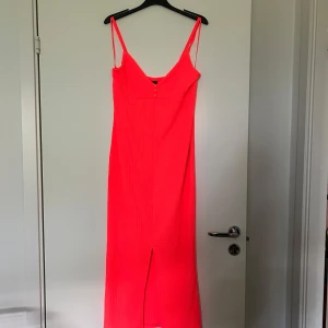 långklänning med knappar - Snygg  långklänning med smala axelband och v-ringning framtill. Klänningen har tre dekorativa knappar vid urringningen och en slits framtill för extra rörelsefrihet. Materialet är lätt strukturerat och känns luftigt, perfekt för varma dagar. Aldrig använd endast provad.