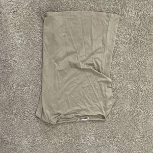 Beige tubtopp från H&M - Enkel och stilren beige tubtopp från H&M. Toppen är axelbandslös och har en rak bandeau-modell i mjukt och stretchigt material, perfekt för varma dagar eller lager på lager. Snygg att matcha med jeans eller kjol.