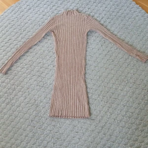 Beige ribbad långärmad klänning - Säljer en beige ribbad klänning med lång ärm och hög hals. Klänningen är figurnära och har en stretchig, stickad känsla som gör den superbekväm. Perfekt för dig som gillar enkel men snygg stil. Den är tight men också väldigt bekväm. Saknar lappen i nacken 