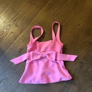 Rosa linnetopp från Zara  - Supersöt rosa linnetopp med breda axelband och en stor rosett framtill som ger en extra pop till outfiten. Toppen har figurnära passform och lätt utsvängd nederkant. Perfekt för dig som vill sticka ut med en färgglad och lekfull look.