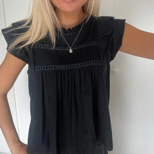 Mörkblå blus med volang och broderi - Supersöt mörkblå blus med volangdetaljer vid axlarna och broderade band över bröstet. Blusen har en lös passform, korta ärmar och liten volang vid halsringningen💓💓🥰