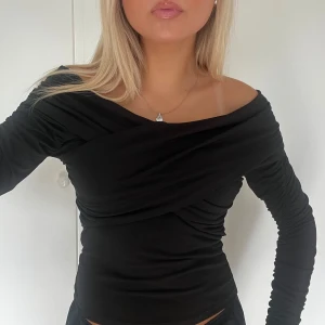 Svart omlott offshoulder topp - Säljer en svart långärmad topp med omlott-detalj och offshoulder-skärning. Snyggt draperad över bysten och figurnära passform🥰