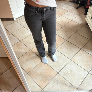 Grå raka jeans från 157 - Säljer ett par svarta  jeans från 157 med raka ben och klassisk femficksdesign. Jeansen har knäppning med knappar, håller på att bli ett hål på innelåret på ena benet (se sista bild). 