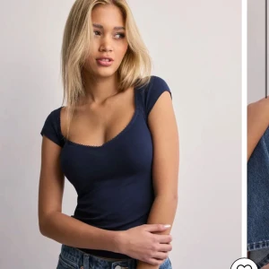 Mörkblå topp med spetskant - Snygg mörkblå topp med korta ärmar och söt spetskant längs den djupa, rundade urringningen. Figurnära passform som framhäver siluetten. Perfekt att matcha med jeans eller kjol för en trendig look.