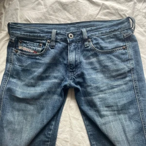 Blå jeans från Diesel - Snygga blå jeans från Diesel med klassisk femficksdesign och låg midja. Jeansen har en bootcut-stil och är perfekta för en avslappnad look. Märkesdetalj på myntfickan ger en extra touch. Det står storlek 26 men skulle säga att det är 32-34 så de är små i storleken.