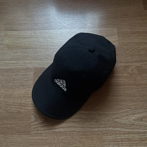 Svart keps från Adidas - Snygg svart keps från Adidas med justerbar rem baktill. Kepsen har en klassisk design med Adidas-logga framtill och är tillverkad i ett lätt och andningsbart material. Använt enstaka gånger 💖