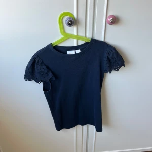 Mörkblå topp med spetsdetaljer - Säljer en mörkblå topp med korta ärmar och vackra spetsdetaljer. Perfekt för en stilren och elegant look. Toppen har en rund halsringning och är tillverkad i ett mjukt material. Storlek 158-164 men passar xs💗