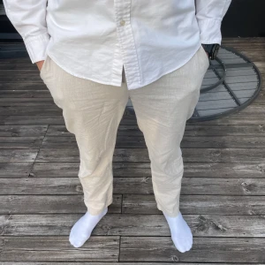 Beige linnebyxor - Snygga beige linnebyxor från Dressmann med en avslappnad passform. Perfekta för varma dagar med sitt lätta och luftiga material. Byxorna har en klassisk design som passar till många olika stilar. Modellen är 185cm lång och väger 82kg. (Lite korta för 185cm)