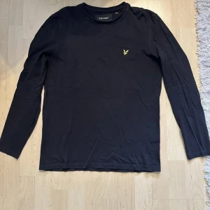 Lyle & Scott svart långarmad tröja - Säljer en stilren svart långärmad tröja från Lyle & Scott med deras ikoniska gula logga på bröstet. Perfekt för en avslappnad och snygg look. Tröjan är i en mjuk och bekväm bomullsmix.