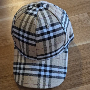 Rutig keps från Burberry - Snygg rutig keps från Burberry i klassiskt beige, svart och vit mönster. Perfekt för att ge din outfit en stilren touch. Justerbar passform för optimal komfort.