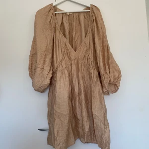 Beige oversize  klänning från H&M - Säljer en snygg  luftig ovesize beige klänning från H&M med v-ringning och långa ärmar. Klänningen har en avslappnad passform och är perfekt för varma dagar. Materialet är lätt och bekvämt.