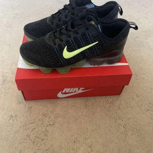 Nike Vapormax i svart och neongul - Snygga Nike Vapormax sneakers i svart med neongula detaljer. Skorna har en stickad ovandel och en unik sula med synliga luftkuddar för extra komfort. Perfekta för både träning och vardag. Kan diskutera pris