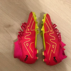 Nike mercurial superfly  - Snygga fotbollsskor från Nike i en iögonfallande rosa och gul färgkombination. Skorna har snörning och en strömlinjeformad design med Nike-loggan på sidan. Perfekta för att dominera på planen med stil.
