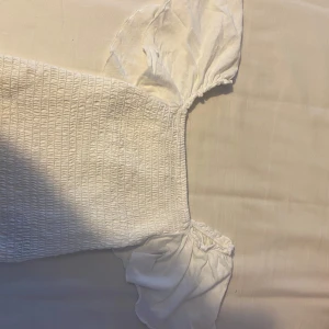 Vit ribbad topp från Kappahl - Säljer en söt vit ribbad topp från Kappahl med puffiga korta ärmar. Perfekt för en somrig look. Toppen har en elastisk passform som gör den bekväm att bära.