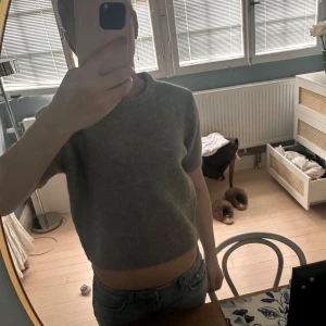 Grå stickad tröja från Zara - Säljer en stilren grå stickad tröja från Zara. Tröjan är lite kortare med korta ärmar och har en mjuk och bekväm känsla. Perfekt för en avslappnad look. Passar bra till jeans eller kjol.