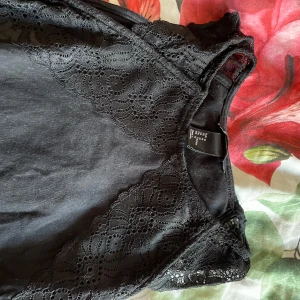 Svart spetsdetaljerad topp från H&M - Säljer en elegant svart topp från H&M med vackra spetsdetaljer. Toppen är ärmlös och har en stilren design som passar perfekt för olika tillfällen. Perfekt för dig som vill ha något stilrent och snyggt i garderoben.