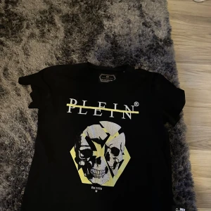 Svart t-shirt från Philipp Plein - Snygg svart t-shirt från Philipp Plein med ett dödskalletryck i vitt och gult på framsidan. T-shirten har korta ärmar och en normal passform. Perfekt för dig som vill sticka ut med stil! Säljer denna riktigt feta pp tröjan som endast använd 5 gånger , några frågor eller funderingar skriv privat🙌 Mvh Eldin