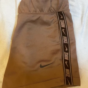 Beige shorts från Nike - Snygg beige shorts från Nike med elastisk midja och logotypband längs sidan. Perfekt för en sportig look. Shortsen  har en kort längd och är gjord i ett bekvämt material.