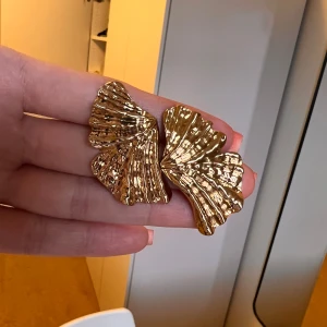 Guldörhängen i form av blad - gina tricot - Säljer ett par eleganta guldörhängen formade som blad. De har en vacker, veckad design som ger en unik och stilfull look. Perfekta för att lyfta vilken outfit som helst.