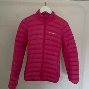 Rosa dunjacka från Everest - Säljer en snygg rosa dunjacka från Everest. Jackan har en dragkedja framtill och är perfekt för kyligare dagar. Den är lätt och smidig att bära med sig. Passar perfekt för både vardag och utomhusaktiviteter.