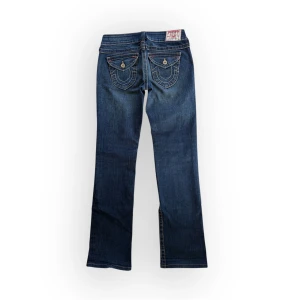 Mörkblå True Religion bootcut jeans - Snygga mörkblå jeans med unika broderade fickor och knappar bak. De har en klassisk femficksdesign och en knappgylf. Perfekta för en avslappnad stil. Storlek W28 vilket motsvarar S. Midja 41, innerben 80. Inga synliga defekter