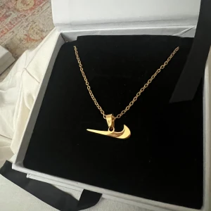 Guldhalsband med Nike-logga - Snyggt guldhalsband med en hängande Nike-logga. I stainless-steel (rostfritt stål) Perfekt skick, oanvänd. Råkade köpa 2 st. Kedjan är tunn och elegant, och loggan är inte så stor vilket gör den lätt att bära till olika tillfällen. 💕