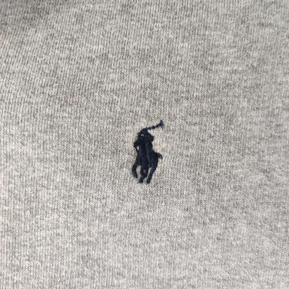 Säljer en stilren grå hoodie från Ralph Lauren med dragkedja och en liten logga på bröstet. Perfekt för en avslappnad look. Den har en mjuk insida och en praktisk huva.. Neuletakit & Villapaidat.