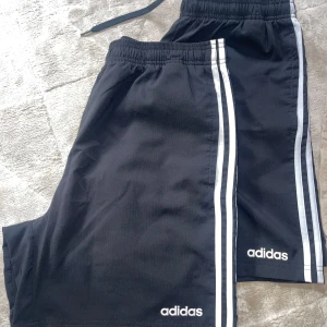 Svarta shorts från Adidas - Snygga svarta shorts från Adidas med de klassiska tre ränderna i vitt längs sidorna. Perfekta för träning eller en avslappnad dag. Elastisk midja för extra komfort.Helt nya! St L . Kom med bud! 
