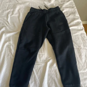 Svarta mjukisbyxor från Nike - Säljer ett par svarta mjukisbyxor från Nike med dragsko i midjan och en diskret logga på benet. Byxorna har en bekväm passform och är perfekta för en avslappnad stil. De har även praktiska fickor på sidorna.